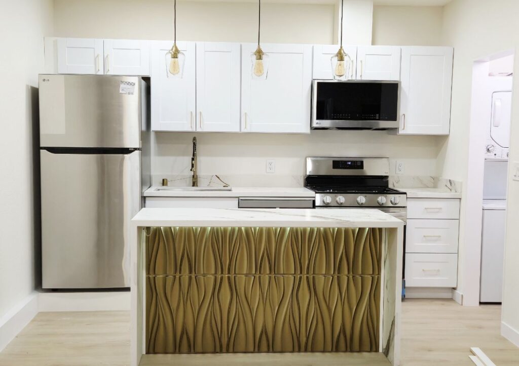 A modern kitchen with white cabinets, stainless steel appliances, and a center island featuring a gold 3D textured design with hidden lighting.