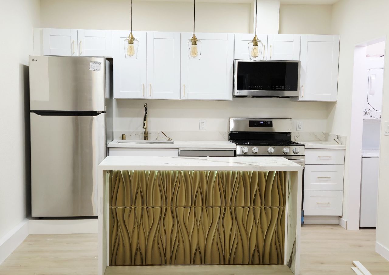 A modern kitchen with white cabinets, stainless steel appliances, and a center island featuring a gold 3D textured design with hidden lighting.